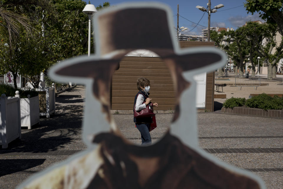 A woman wearing a face mask to protect against coronavirus is pictured through a hole in a cardboard cut out of actor Clint Eastwood in Cannes, southern France, Tuesday, May 12, 2020. The Cannes Film Festival won't kick off as planned on Tuesday. The festival’s 73rd edition has been postponed indefinitely, part of the worldwide shutdowns meant to stop the spread of the coronavirus. (AP Photo/Daniel Cole)