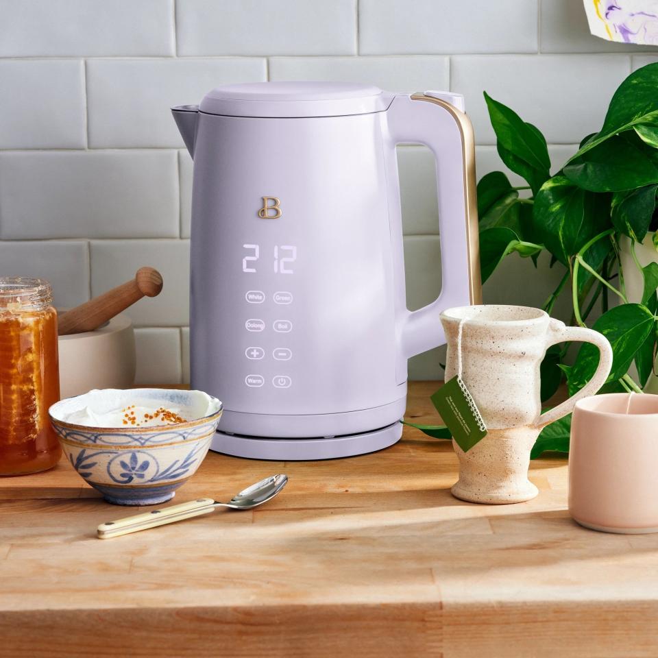 Lavender kettle on a butcher block countertop with various tea accessories around it