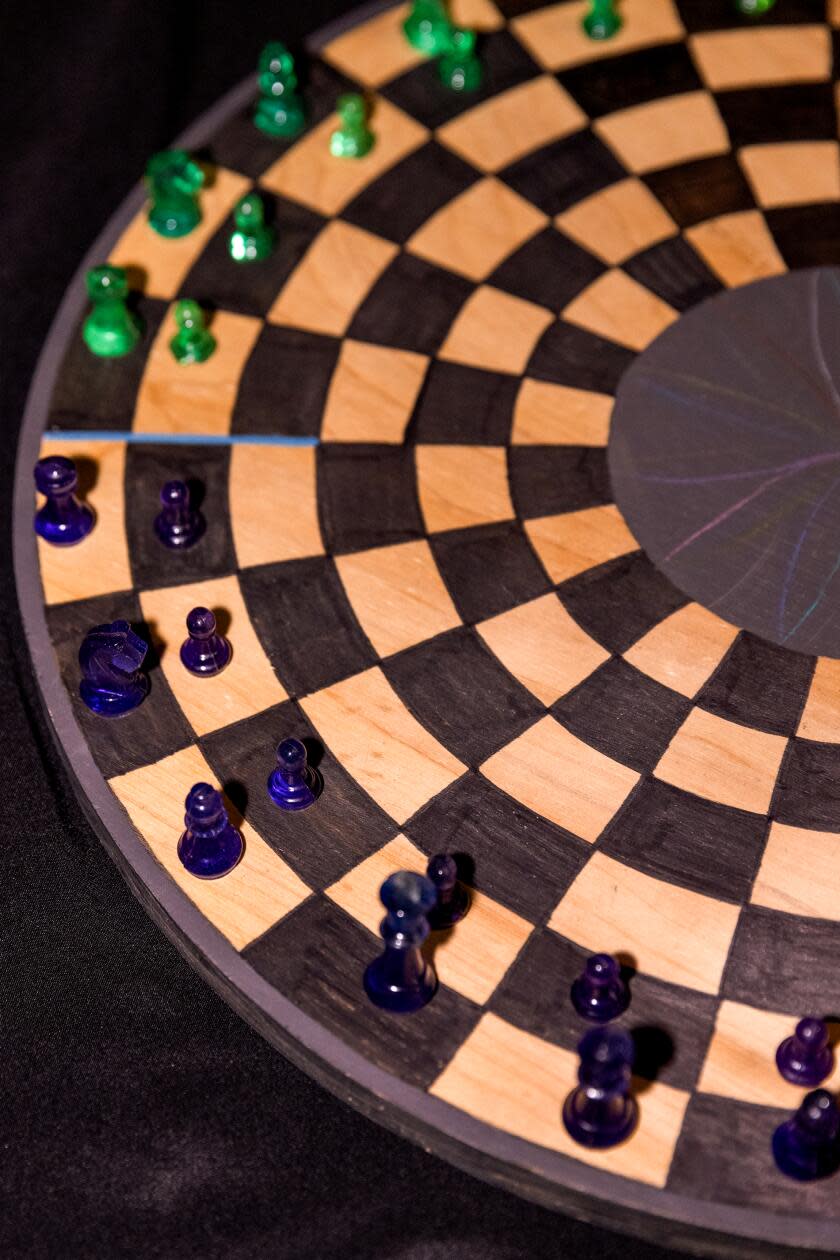 A detail of a circular chess board with black and green pieces on it.