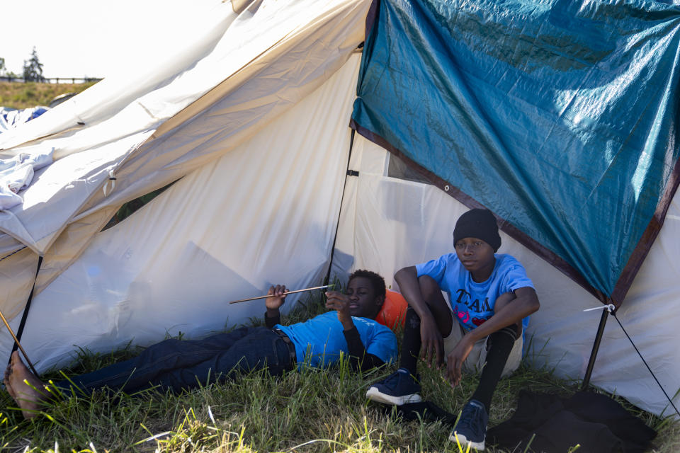 Eduardo Afonso, 15, and Makiese Alexandria Shabani, 10, both of Angola, sit in the shade of a tent at an encampment of asylum-seekers mostly from Venezuela, Congo and Angola next to an unused motel owned by the county, Wednesday, June 5, 2024, in Kent, Washington. The group of about 240 asylum-seekers is asking to use the motel as temporary housing while they look for jobs and longer-term accommodations. (AP Photo/Lindsey Wasson)