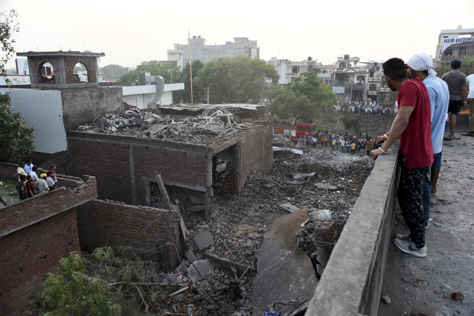 People watch rescuers work at the site of an explosion at a fireworks factory in Batala, in the northern Indian state of Punjab, Wednesday, Sept. 4, 2019. More than a dozen people were killed in the explosion that caused the building to catch fire and collapse, officials said. (AP Photo/Prabhjot Gill)