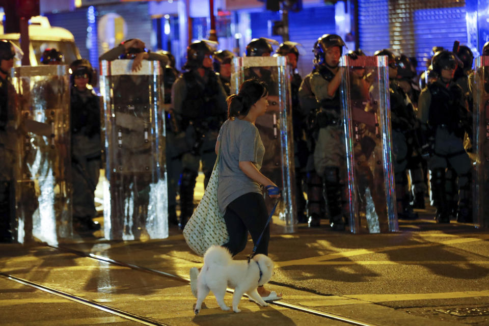 A woman leads her dog past by riot police guarding on a street during an anti-extradition ball protest in Hong Kong, Sunday, Aug. 4, 2019. Another police station in Hong Kong became the target of protesters' ire on Sunday as rallies in two different parts of the city converged into one, with participants gearing up for another night of protracted demonstrations. (AP Photo/Vincent Thian)