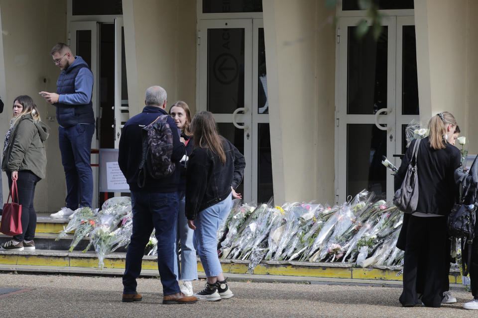 People stand by flowers laid by the Gambetta high school, Monday, Oct. 16, 2023 in Arras, northern France. French authorities say the high school where a teacher was fatally stabbed in an attack last week has been evacuated over a bomb alert, as France's President cut short travel plans abroad to host a security meeting Monday. (AP Photo/Michel Spingler)