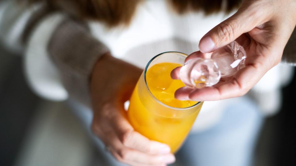 Woman putting ice cubes into orange electrolyte drink