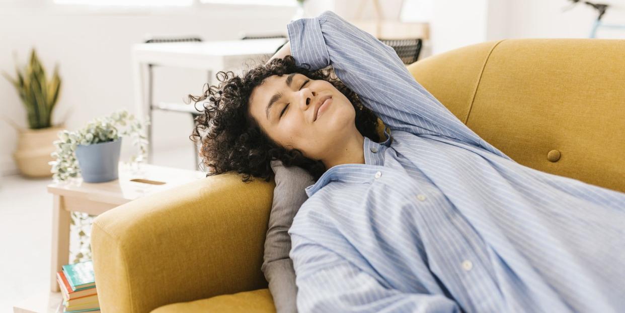 smiling young woman with eyes closed resting on sofa at home