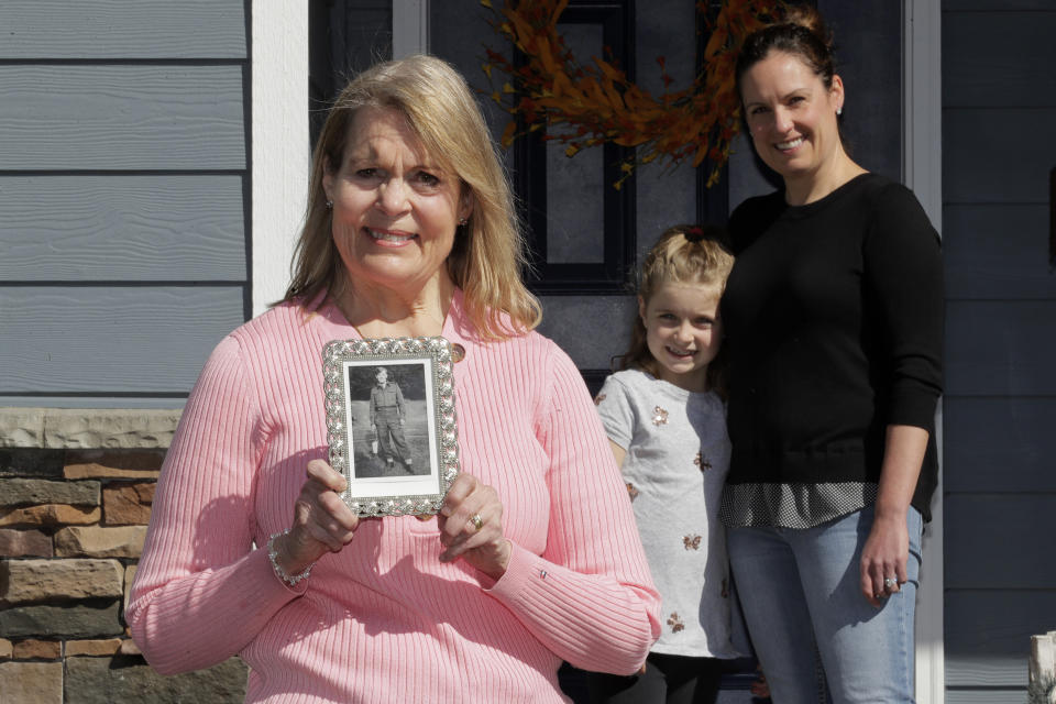 In this Wednesday, April 8, 2020, photo, Patty Cooper, left, poses for a photo as she holds a family photograph of her father, Bill Chambers, when he was in his late teens and a member of the Canadian Army, as Cooper's daughter Kelly Adsero, right, and granddaughter Molly look on, in Woodinville, Wash. Chambers, 97, died March 14, 2020, at an adult family home where he lived with four other World War II veterans. He wasn't obviously ill, but tested positive for the new coronavirus after he died. (AP Photo/Ted S. Warren)