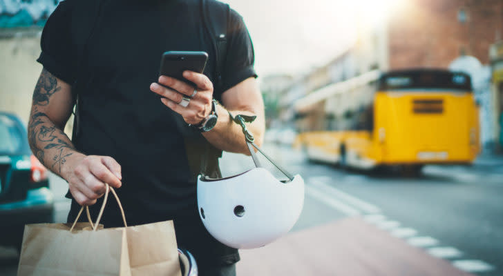 A tattooed person is holding a paper bag, a bicycle helmet and a cellphone.