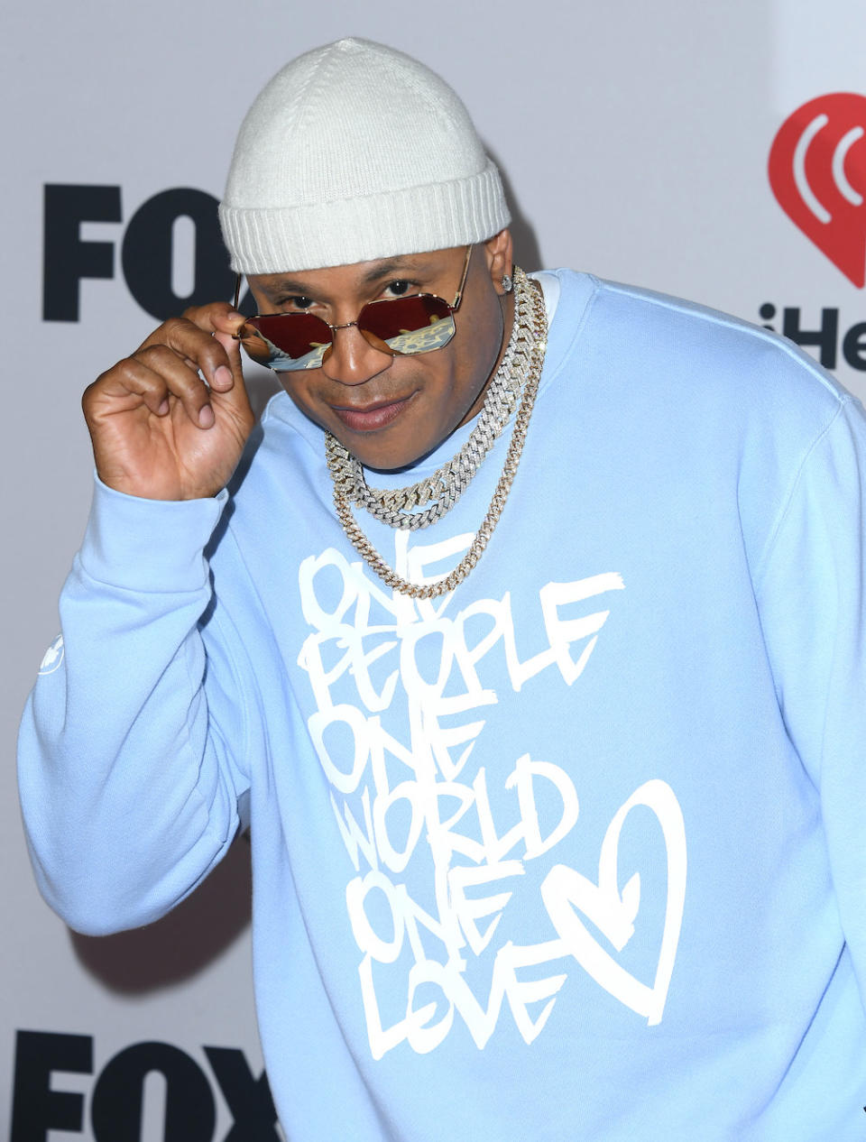 LL in a cap, glasses, thick chain necklaces, and sweatshirt that says "One people one world one love"