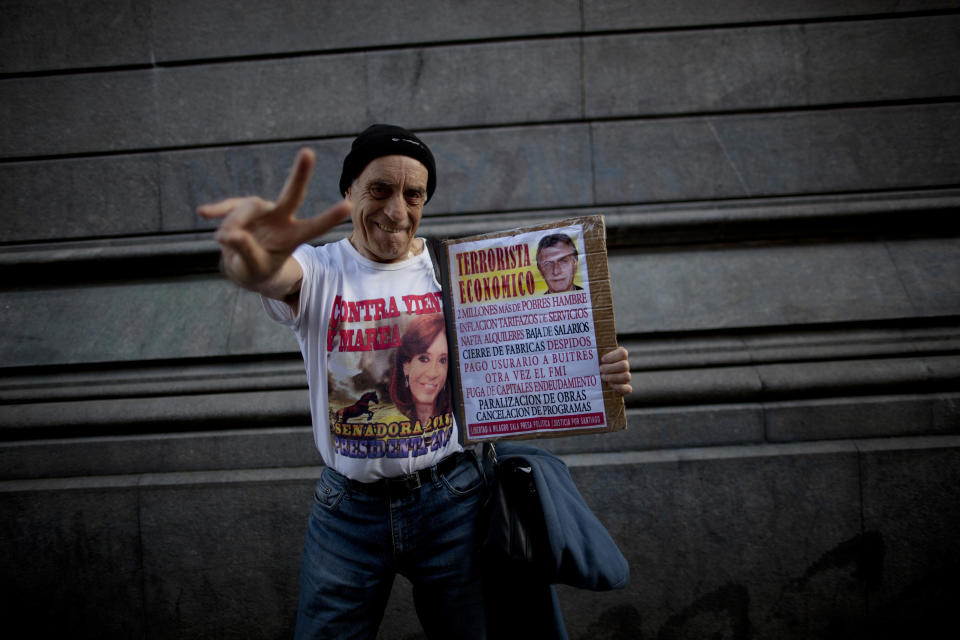 In this Oct. 3, 2018 photo, philosophy professor Juan Carlos Amarfil, 67, strikes a pose wearing a T-shirt emblazoned with an image of former President Cristina Fernandez, as he holds a poster headlined, "Economic terrorist" next to an image of President Maurcio Macri, during a demonstration demanding improved conditions for disabled retirees, in Buenos Aires, Argentina. Cries of support for Fernandez, who is now serving as a senator, continue to rise from crowds during protests against the austerity policies of Macri, the conservative who replaced her as leader of Argentina. (AP Photo/Natacha Pisarenko)