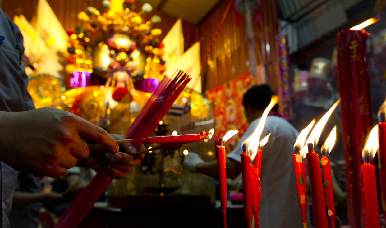 Ethnic Chinese burns joss sticks infront of a 26 foot-high giant paper statue of the Chinese deity 