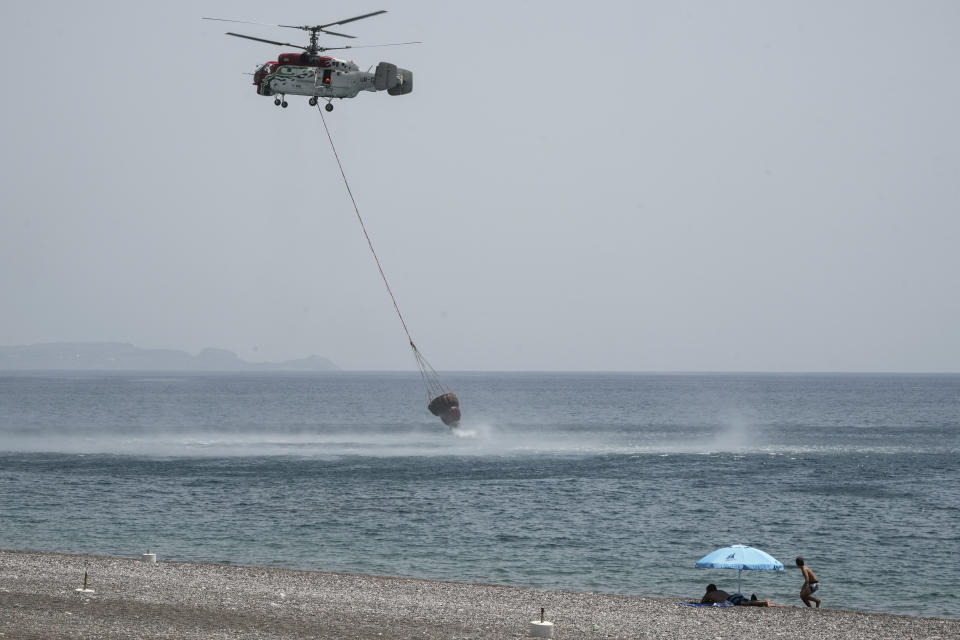 FILE - Beachgoers watch a helicopter filling water from the sea during a wildfire, near Gennadi village, on the Aegean Sea island of Rhodes, southeastern Greece, on July 27, 2023. Tourists at a seaside hotel on the Greek island of Rhodes snatched up pails of pool water and damp towels as flames approached, rushing to help staffers and locals extinguish one of the wildfires threatening Mediterranean locales during recent heat waves. (AP Photo/Petros Giannakouris, File)