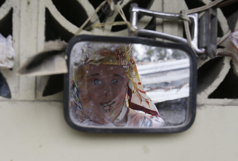 A woman dressed for "La Diablada" festival, sees her reflection on a mirror, in Pillaro, Ecuador, Friday, Jan. 6, 2017. Local legend holds that anyone who adopts a costume for the celebration and wears it at the event six years in a row will have good luck. (AP Photo/Dolores Ochoa)