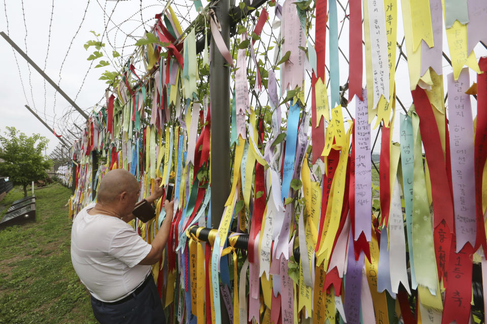 A visitor takes photos through a wire fence decorated with ribbons written with messages wishing for the reunification of the two Koreas at the Imjingak Pavilion, near the demilitarized zone of Panmunjom, in Paju, South Korea, Thursday, June 20, 2019. Chinese President Xi Jinping departed Thursday morning for a state visit to North Korea, where he's expected to talk with leader Kim Jong Un about his nuclear program while negotiations have stalled with Washington. (AP Photo/Ahn Young-joon)