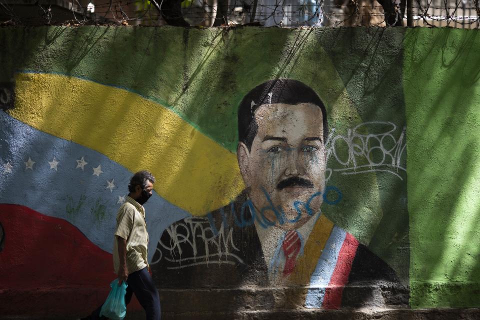 Un individuo que luce un barbijo pasa frente a un mural de Nicolás Maduro en Caracas el 22 de julio del 2020. Maduro sigue firme en el poder más de un año después de que Juan Guaidó se declarase presidente legítimo y recibiese el reconocimiento de EEUU y una cincuentenan de países. (AP Photo/Ariana Cubillos)