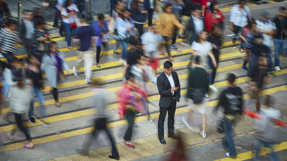 High angle view of businessman using smart phone amidst crowd. Professional is standing on busy street. He is surrounded by people in city