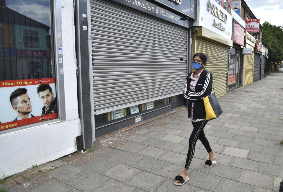 A woman wearing a mask to protect against coronavirus, walks in Melton Road also known as the Golden Mile in Leicester, England, Tuesday June 30, 2020. The British government has reimposed lockdown restrictions in the English city of Leicester after a spike in coronavirus infections, including the closure of shops that don't sell essential goods and schools. (AP Photo/Rui Vieira)