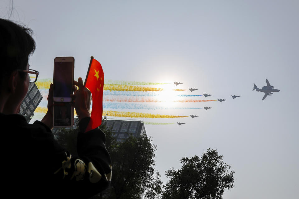 A man uses his smartphone to film Chinese military planes trail colored smoke as they fly in formation past the sun during a parade to commemorate the 70th anniversary of the founding of Communist China in Beijing, Tuesday, Oct. 1, 2019. China's Communist Party is celebrating its 70th anniversary in power with a parade showcasing its economic development and newest weapons. The event marks the anniversary of the Oct. 1, 1949, announcement of the founding of the People's Republic of China by then-leader Mao Zedong. (AP Photo/Andy Wong)