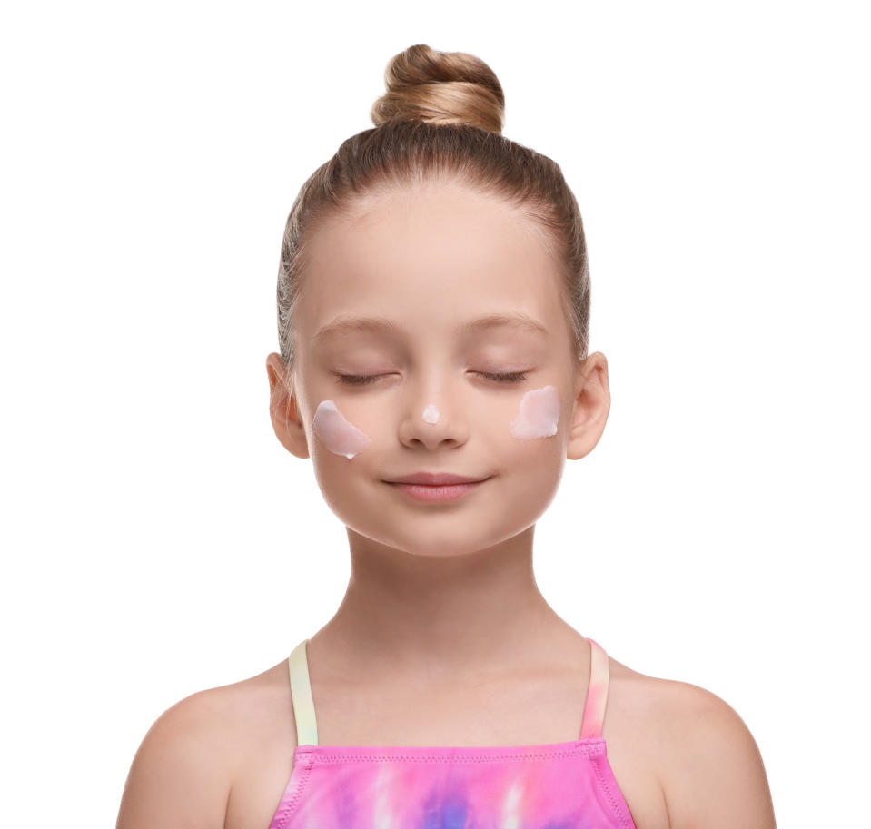 Girl with closed eyes and sunscreen on cheeks wears a shiny pink top