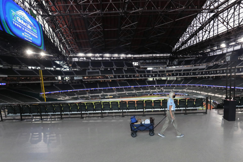 A Texas Rangers employee pulls a cart down an empty concourse at Globe Life Field, home of the Texas Rangers baseball team, in Arlington, Texas, Monday, June 1, 2020. It used to be that empty seats caused palpitations in team owners and college administrators relying on ticket sales and concessions to balance the budget. Now, those empty seats, and short lines and clear concourses, will be the norm for a while as sports grapples with social distancing requirements in the age of coronavirus. (AP Photo/LM Otero)