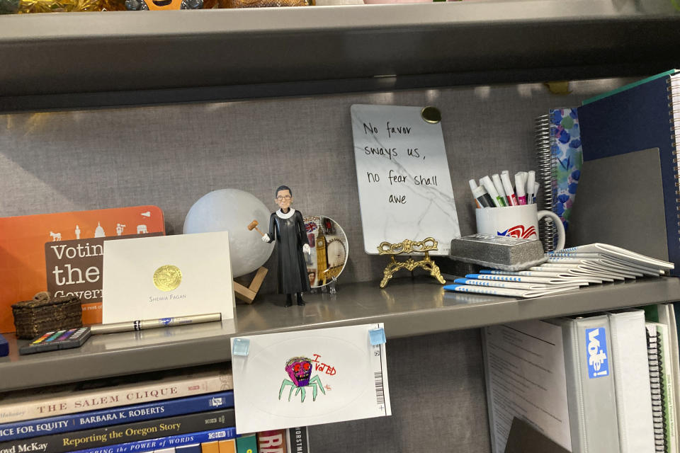 A bookshelf in the cubicle of Oregon elections investigator Alma Whalen displays an inspirational slogan that once adorned an Oregon newspaper: "No favor sways us, no fear shall awe," in Salem, Ore., on Oct. 17, 2022. Whalen says she the elections division is seeing more requests for investigations and is facing pressure from people to come up with a decision that favors them. (AP Photo/Andrew Selsky)