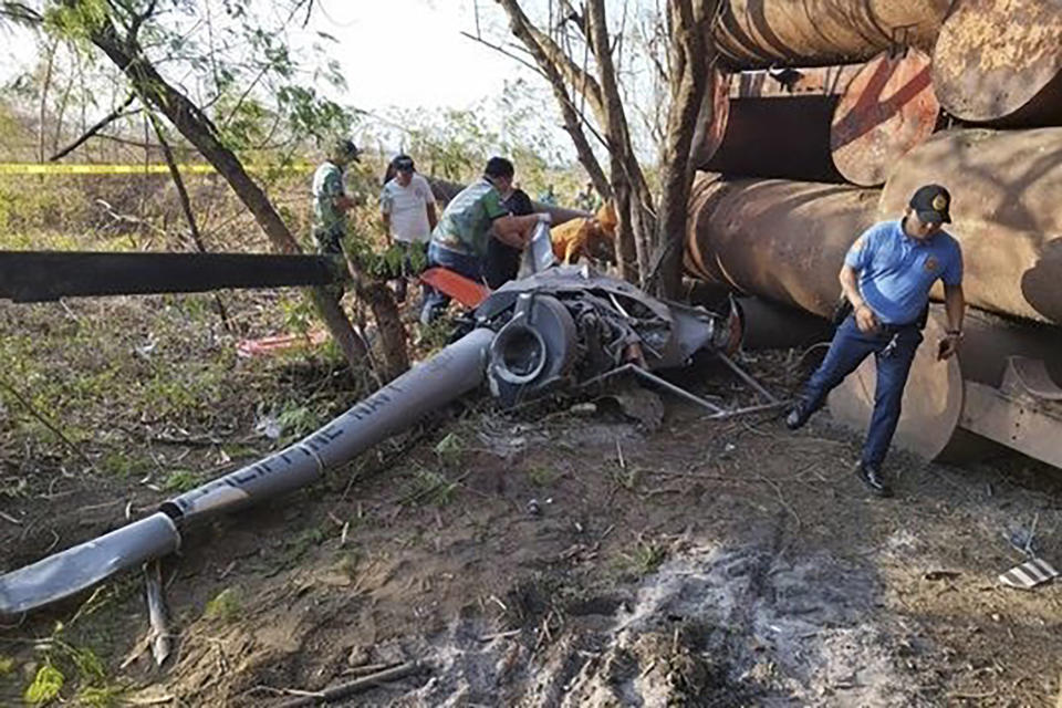 In this handout photo provided by the Cavite Police Regional Office 4A, rescuers check the remains of a trainer helicopter after it crashed in Cavite province, Philippines on Thursday, April 11, 2024. A Philippine Navy helicopter crashed in a grassy area near a public market, killing two pilots on board, the military and police said. (Cavite Police Regional Office 4A via AP)