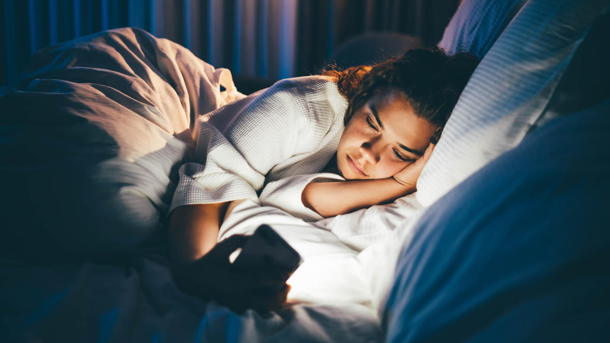  A woman wakes up for the fourth time during the night and lies in bed staring at her phone, unable to sleep. 