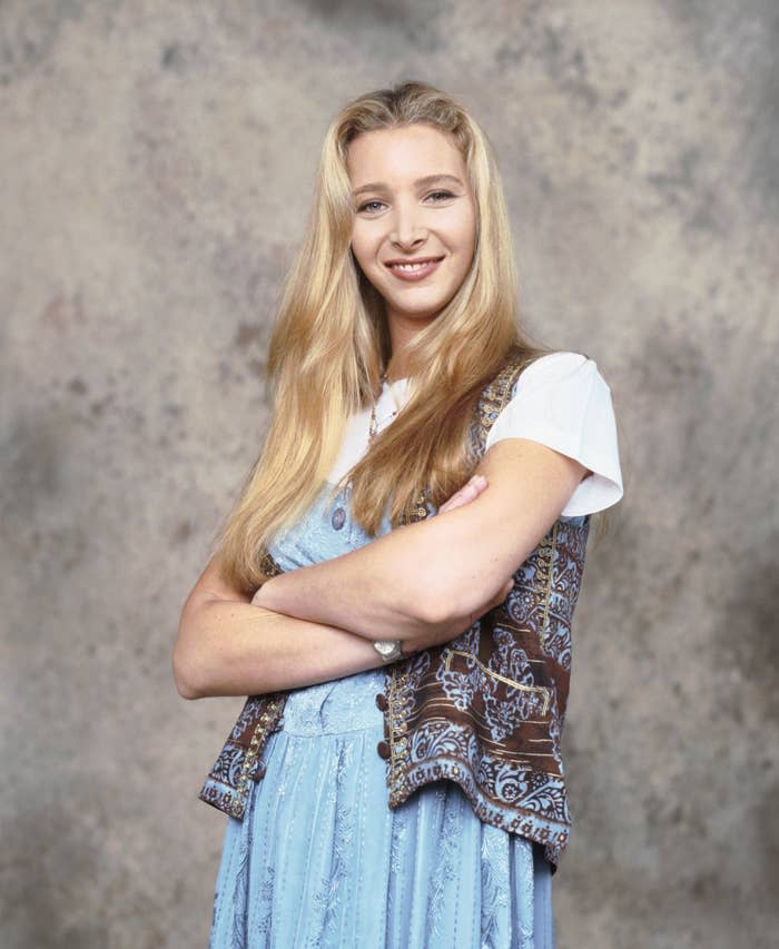 Lisa Kudrow smiling with arms crossed, wearing a white shirt under a patterned vest and a light dress