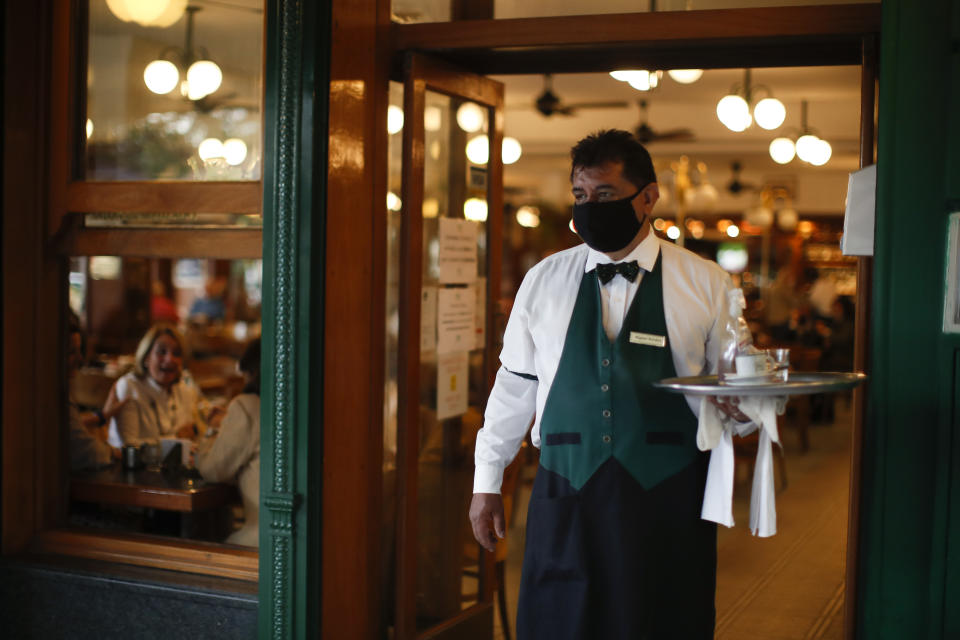 El camarero Miguel Bordon lleva una taza de café a un cliente en el café La Biela en Buenos Aires, Argentina, el martes 10 de noviembre de 2020. (AP Foto/Natacha Pisarenko)