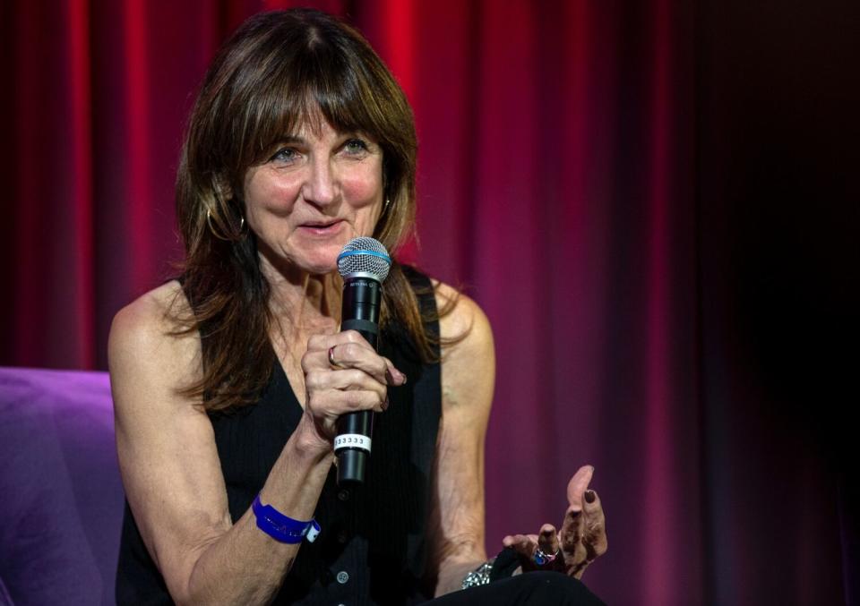 A seated, smiling woman speaks into a microphone.