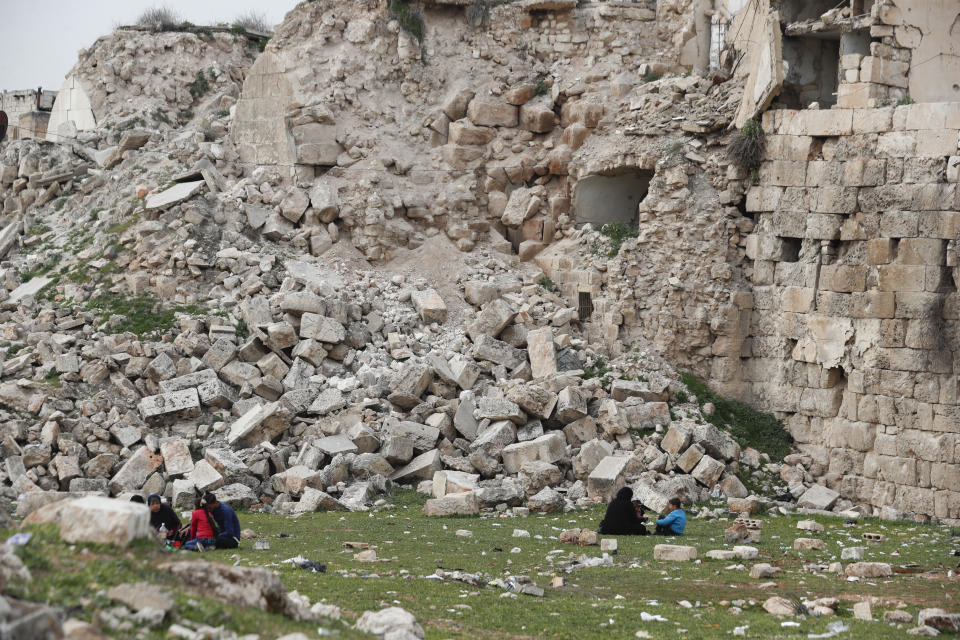 People sit by a building destroyed in recent earthquake in Aleppo, Syria, Monday, Feb. 27, 2023. (AP Photo/Omar Sanadiki)