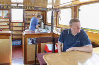 John Collier sits in the saloon while his brother Danny makes tea in the kitchen aboard their boat, the Princess Freda on the river Thames in London, Friday, May 8, 2020. The brothers are the proud owners of the boats the Princess Freda, the Queen Elizabeth, the Connaught and the Clifton Castle. All four boats have had their moment in the sun. And all four were meant to have another on Friday as Britain celebrates the 75-year anniversary of Victory in Europe Day. Instead, they're lying idle on the banks of the River Thames, not far from Kew Gardens in southwest London, as the festivities surrounding VE Day have been all but cancelled as a result of the coronavirus pandemic. For the brothers it’s nothing less than a disaster, one that could spell the demise of the company their late father created in 1975. (AP Photo/ Vudi Xhymshiti)