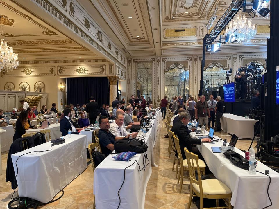 rows of long white tables with press members sitting behind them