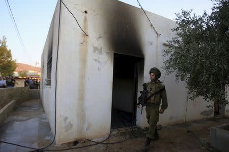 An Israeli soldier walks past a house that had been torched in a suspected attack by Jewish extremists killing an 18-month-old Palestinian child, injuring a four-year-old brother and both their parents at Kafr Duma village near the West Bank city of Nablus July 31, 2015. REUTERS/Abed Omar Qusini