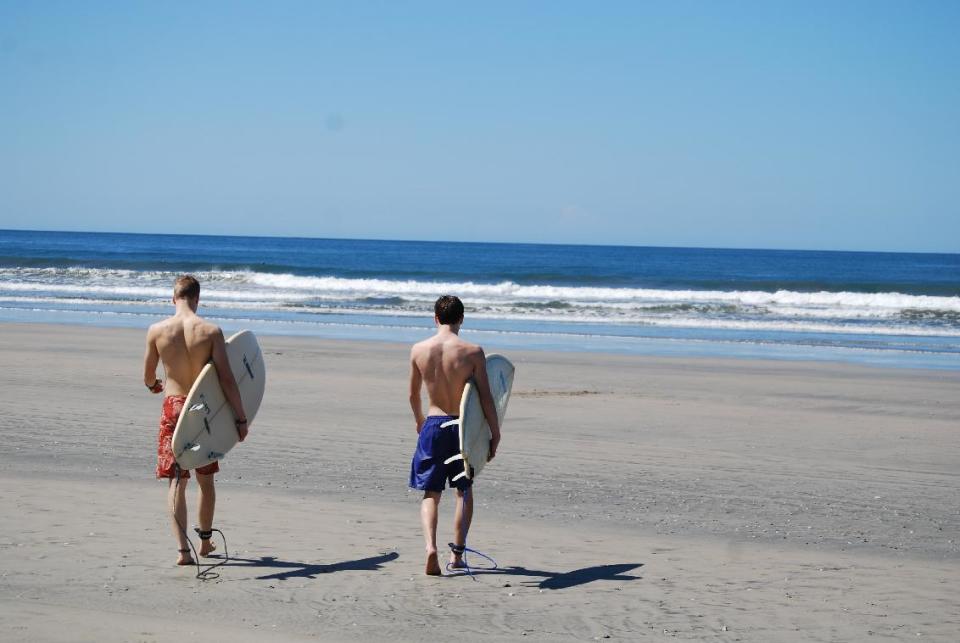 This February 2014 photo released by Kristina MacKulin shows Liam Godfrey-Jolicoeur and Jacob Dombek, of N. Ferrisburg, Vt., heading out to surf at Playa Guiones in Nosara, Costa Rica. Nosara is a scenic coastal region with a variety of outdoor recreation activities for visitors. (AP Photo/Kristina MacKulin)