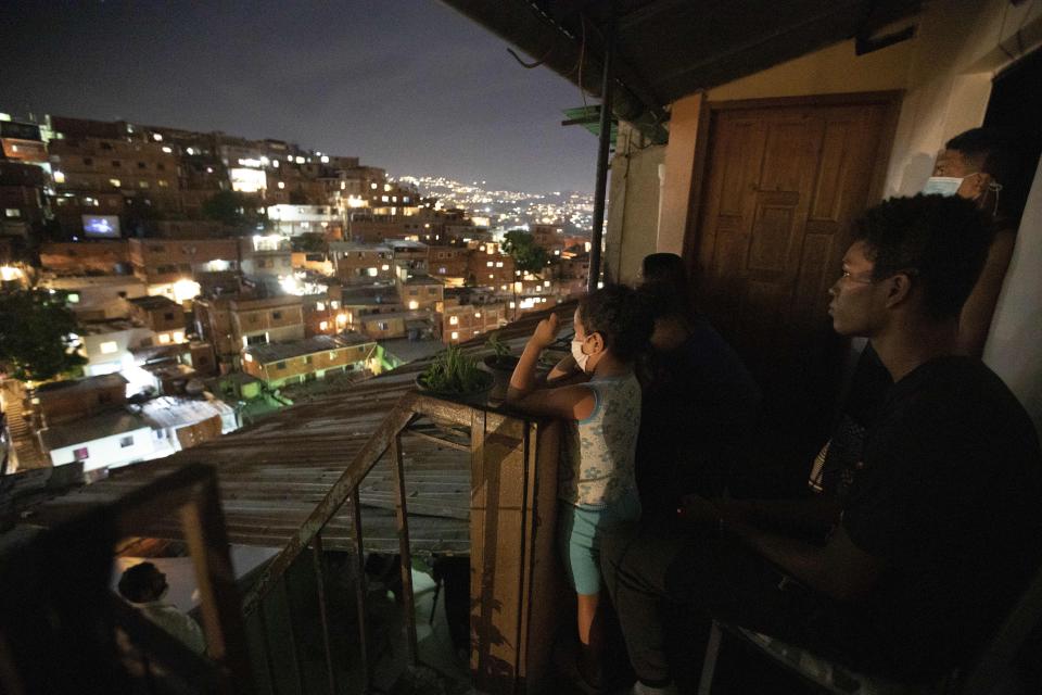 People watch the movie Aladdin projected across the street on the roof of a home, left, in the Petare neighborhood of Caracas, Venezuela, late Monday, June 1, 2020. A neighborhood group called The Download Zone set up the movie as a free entertainment option for families cooped up since mid-March under the COVID-19 quarantine. (AP Photo/Ariana Cubillos)