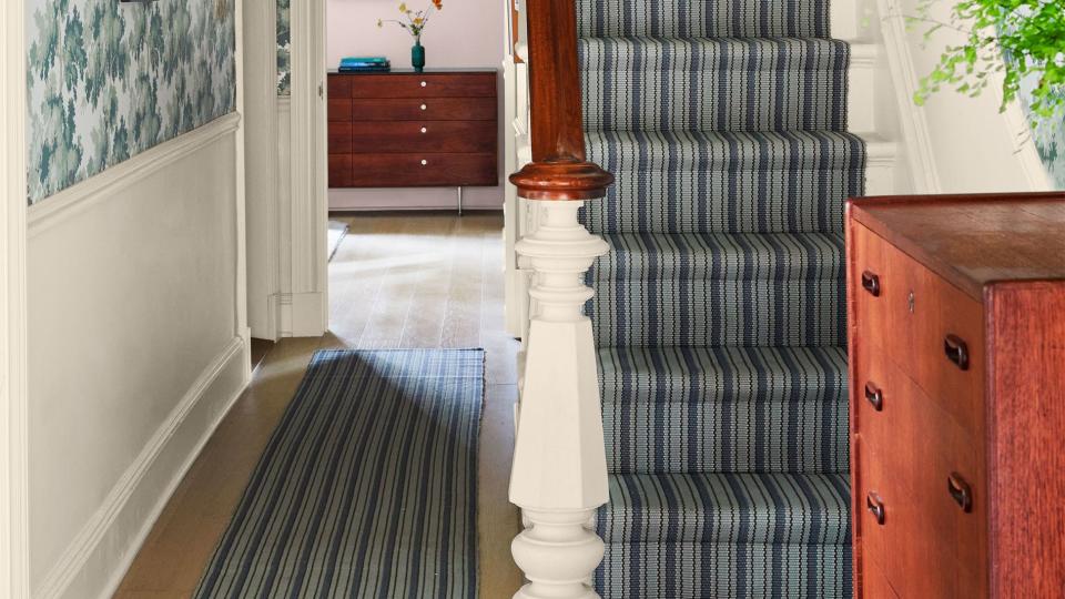 hallway with striped runner on floor and stairs leading up with matching striped fabric and on the walls is a very verdant wallpaper