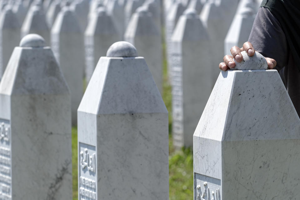 A woman touches a grave stone in Potocari, near Srebrenica, Bosnia, Saturday, July 11, 2020. Mourners converged on the eastern Bosnian town of Srebrenica for the 25th anniversary of the country's worst carnage during the 1992-95 war and the only crime in Europe since World War II that has been declared a genocide. (AP Photo/Kemal Softic)
