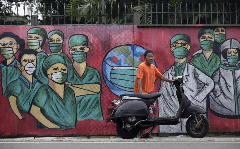 A motorists stops near a mural painted as a tribute to medical workers in Depok, on the outskirts of Jakarta, Indonesia, Wednesday, April 15, 2020. Indonesia's capital kicked off a stricter restriction to slow the spread of the new coronavirus last week as the metropolitan area has become Indonesia's coronavirus epicenter. (AP Photo/Dita Alangkara)