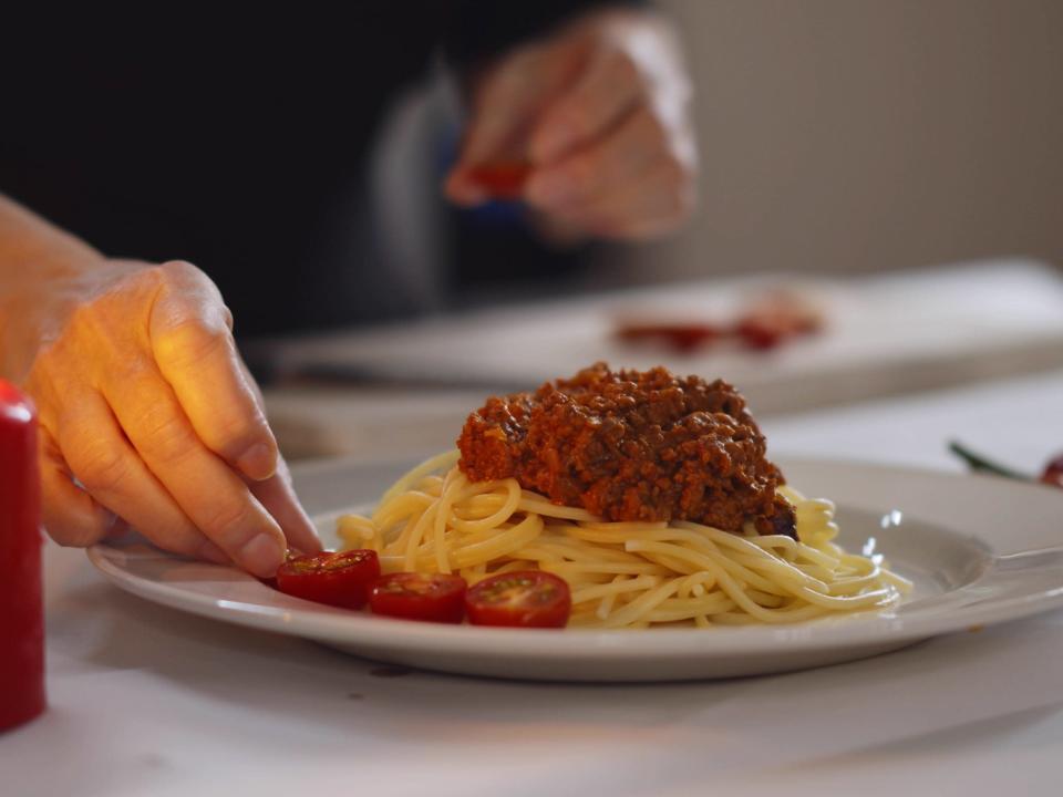 person arranging cherry tomatoes on a pasta plate with a lit candle beside it