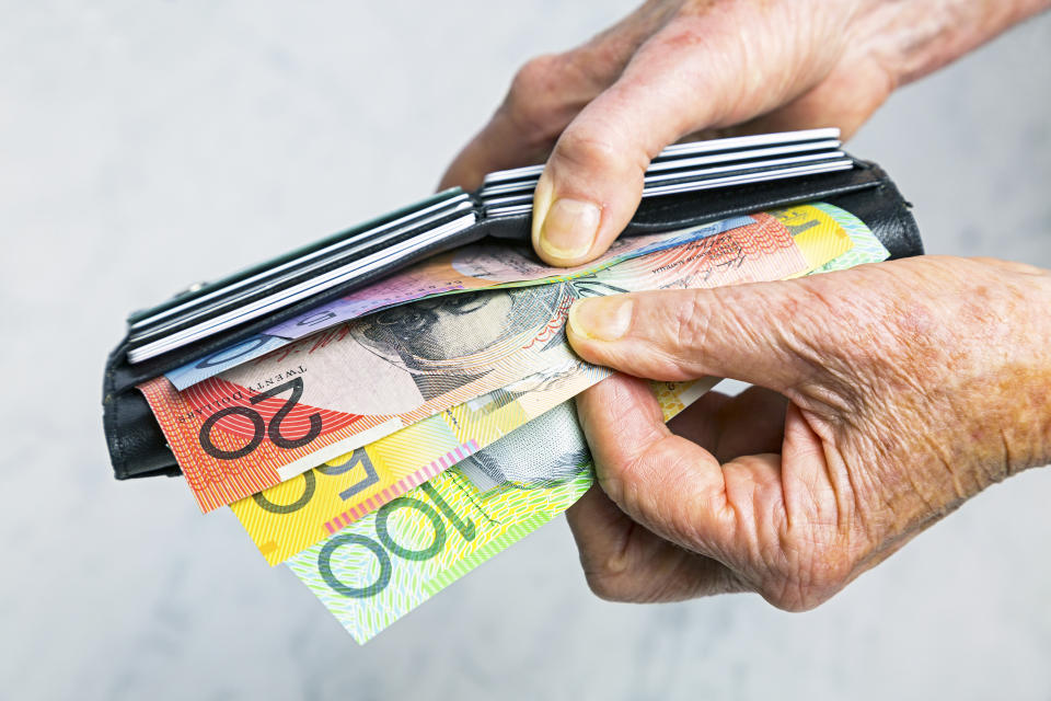 Close-up, senior female hands taking Australian banknotes (cash, currency) from purse containing many credit cards.  Horizontal, studio, copy space.