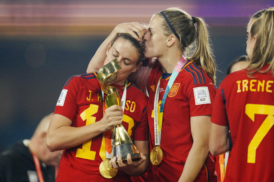 Spain's Alexia Putellas kisses the trophy while getting a kiss herself from teammate Irene Paredes, celebrating at the end of the Women's World Cup soccer final between Spain and England at Stadium Australia in Sydney, Australia, Sunday, Aug. 20, 2023. Spain won 1-0. (AP Photo/Abbie Parr)