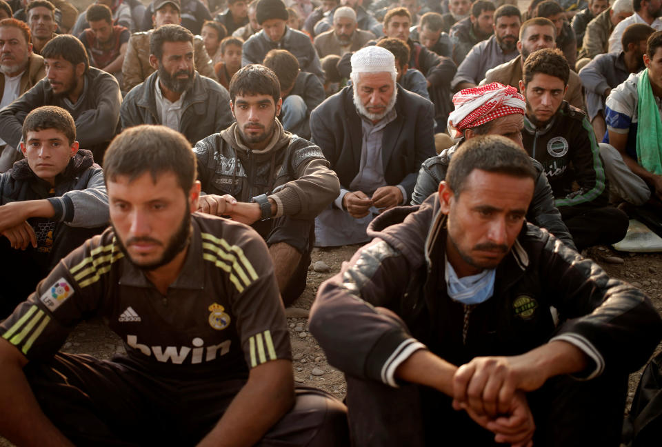 Newly displaced men sit at a check point in Qayyara