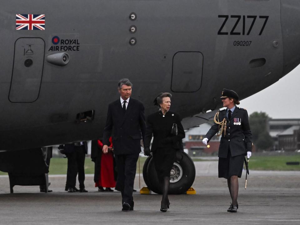 Vice Admiral Timothy Laurence, Princess Anne, and Station Commander Group Captain McPhaden walk in front of the plane that transferred Queen Elizabeth from Scotland to England.