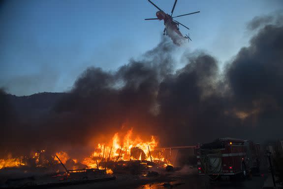 A water-dropping helicopter drops its load onto burning homes at Rancho Monserate Country Club.