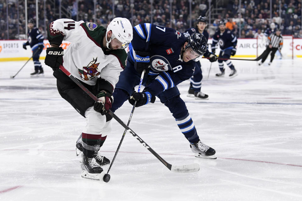 Arizona Coyotes defenseman Shayne Gostisbehere (14) and Winnipeg Jets center Adam Lowry (17) battle for the puck during second-period NHL hockey game action in Winnipeg, Manitoba, Sunday, Jan. 15, 2023. (Fred Greenslade/The Canadian Press via AP)