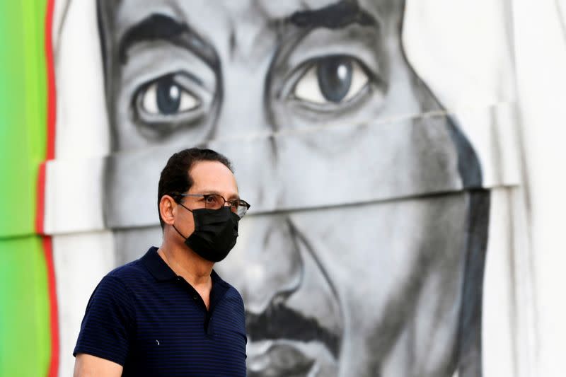 FILE PHOTO: A Saudi man walks past a poster depicting Saudi King Salman bin Abdulaziz, after a curfew was imposed to prevent the spread of the coronavirus disease (COVID-19), in Riyadh