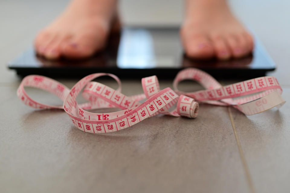 Young adult woman measuring herself on a scale put weight. Source: Getty Images