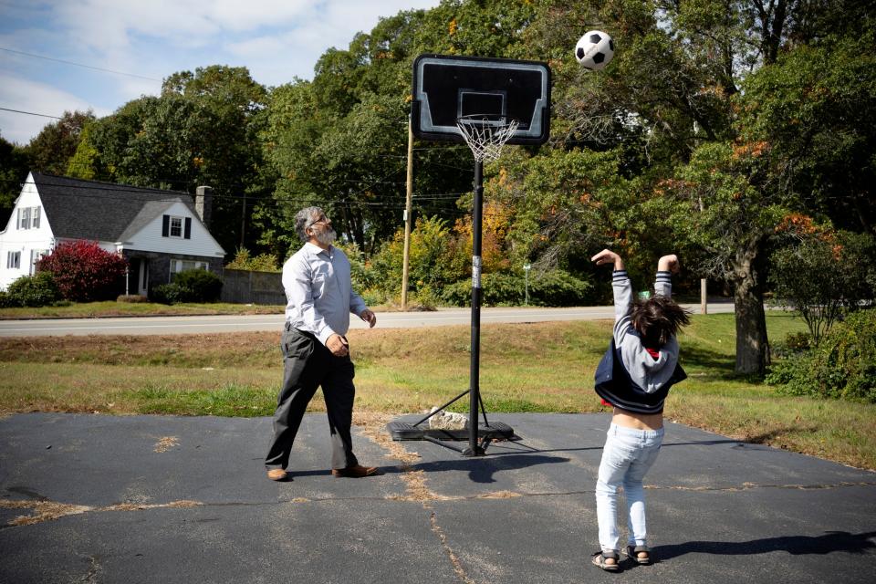 A man and a kid play basketball in a suburban driveway.