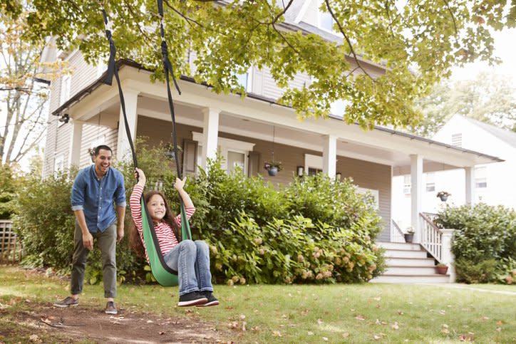 A smiling father pushing his laughing daughter on a tree swing in their front yard.