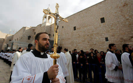A clergyman holds a cross during Christmas celebrations at Manger Square outside the Church of the Nativity in Bethlehem, in the Israeli-occupied West Bank December 24, 2018. REUTERS/Mussa Qawasma